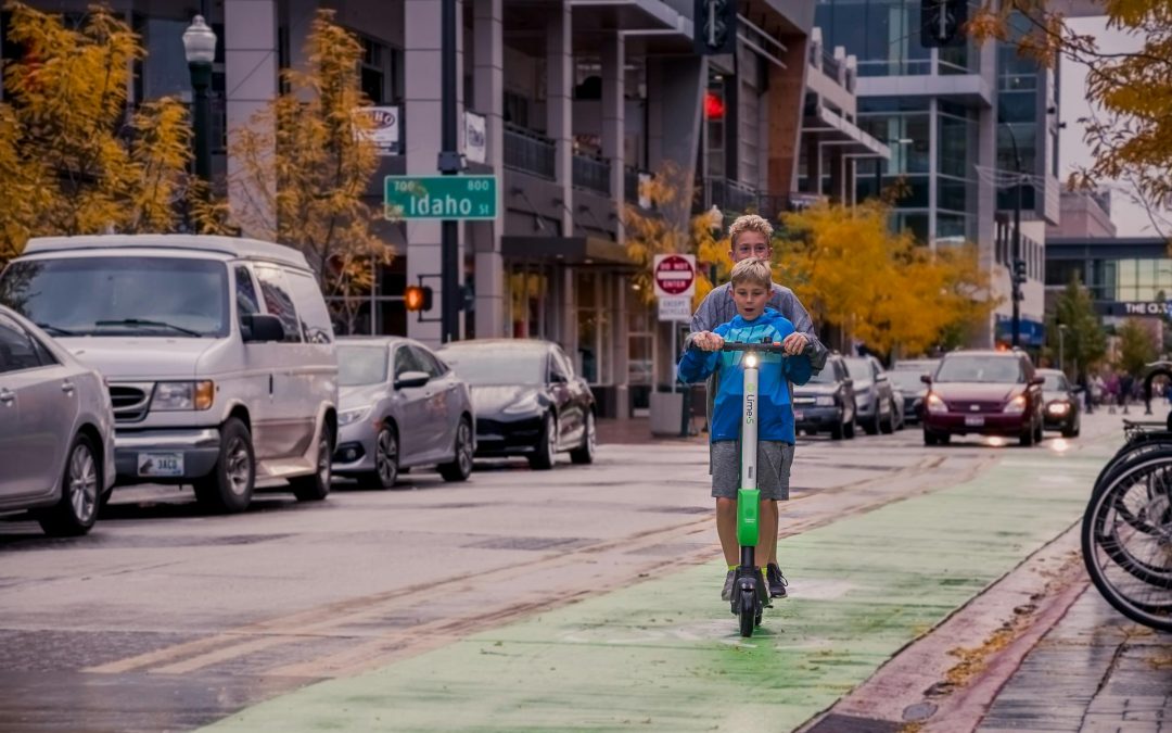 Two Boys Riding Lime-s Scooter On Street